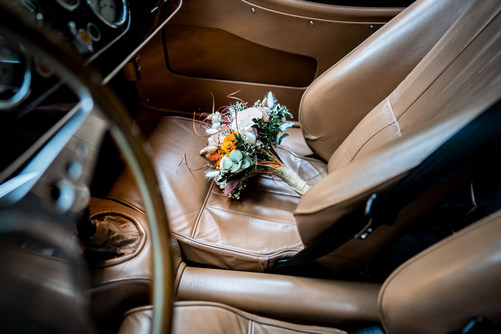 Beau bouquet de fleurs blanches et roses posé sur le siège en cuir d'une voiture de collection, photographie de mariage élégante capturée par le photographe professionnel Dis-moi Oui. Décor romantique pour une journée inoubliable